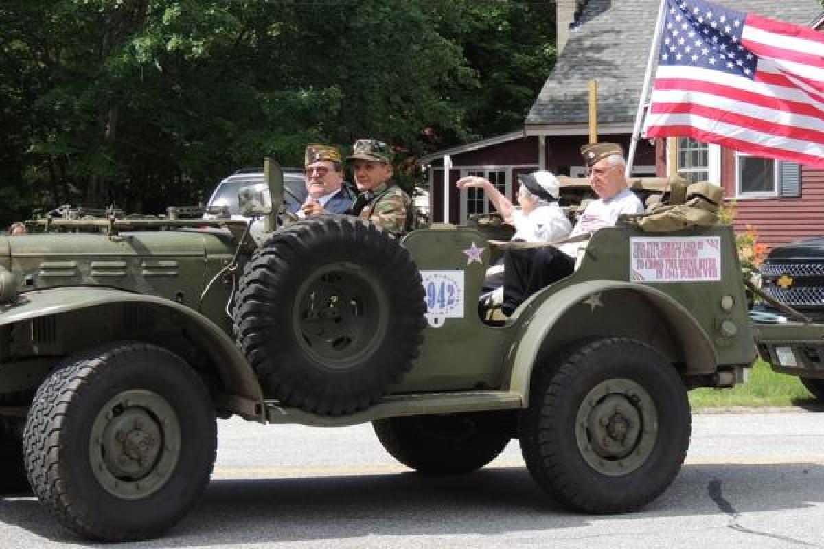 4th of July parade - soldiers driving military vehicle, elderly couple in back set - American flag attached to back, flying.